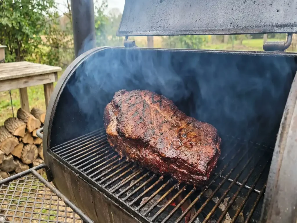 Smoked brisket on smoker grate during low and slow cook with bark forming
